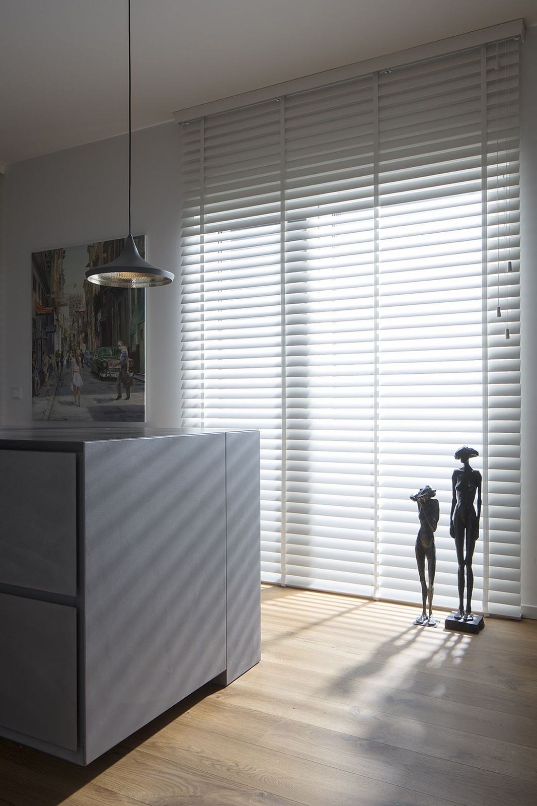 Estores laminados brancos num envidraçado alto, a filtrar a luz sobre o soalho